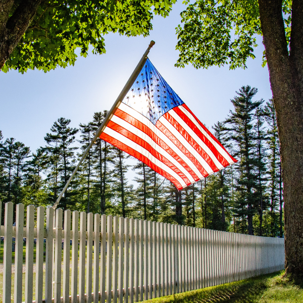 Sunlit American flag over white picket fence